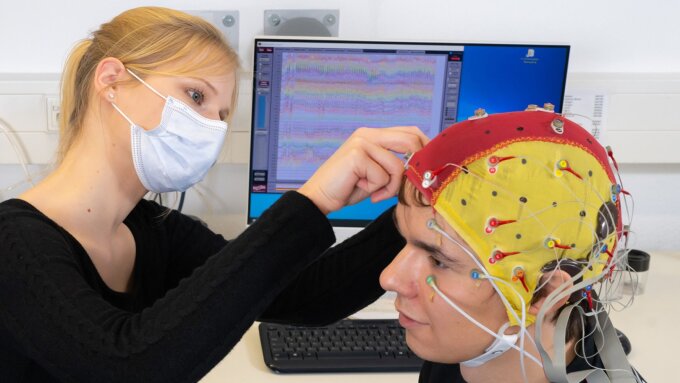 Doktorandin Celina von Eiff befestigt für die EEG-Studie mit Cochlea-Implantaten Elektroden an der Kappe eines Probanden.