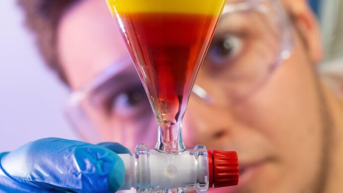 Nikolai Löhr, Doktorand der Arbeitsgemeinschaft Pharmazeutische Mikrobiologie und Erstautor der Studie, zeigt Anthrachinon-Verbindungen im organischen Lösungsmittel in einem Versuchsaufbau.
