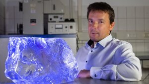 Glass chemist Prof. Dr. Lothar Wondraczek next to a glass block consisting of high-purity borosilicate glass in the laboratory.