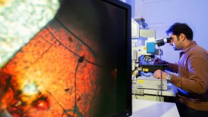 Doktorand Vahid Nozari untersucht an einem Mikroskop das neue synthetische Glas.
