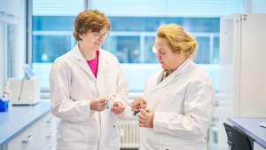 Prof. Dr Rosalind Allen and Dr Anne Busch stand in the laboratory holding a urinary catheter in their hands.