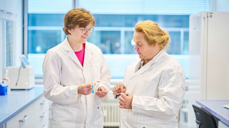 Prof. Dr Rosalind Allen and Dr Anne Busch stand in the laboratory holding a urinary catheter in their hands.